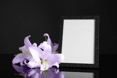 Funeral photo frame and violet lilies on table against black background