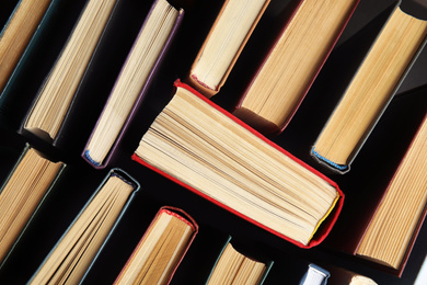 Photo of Many different hardcover books on dark background, top view