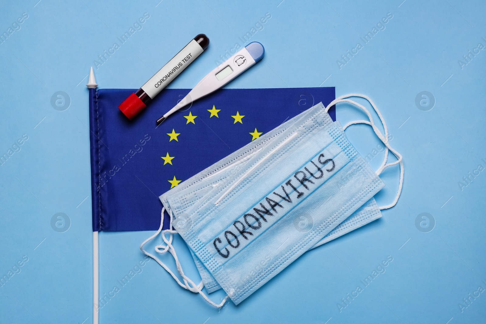 Photo of European Union flag, protective masks, thermometer and test tube with blood sample on light blue background, flat lay. Coronavirus outbreak