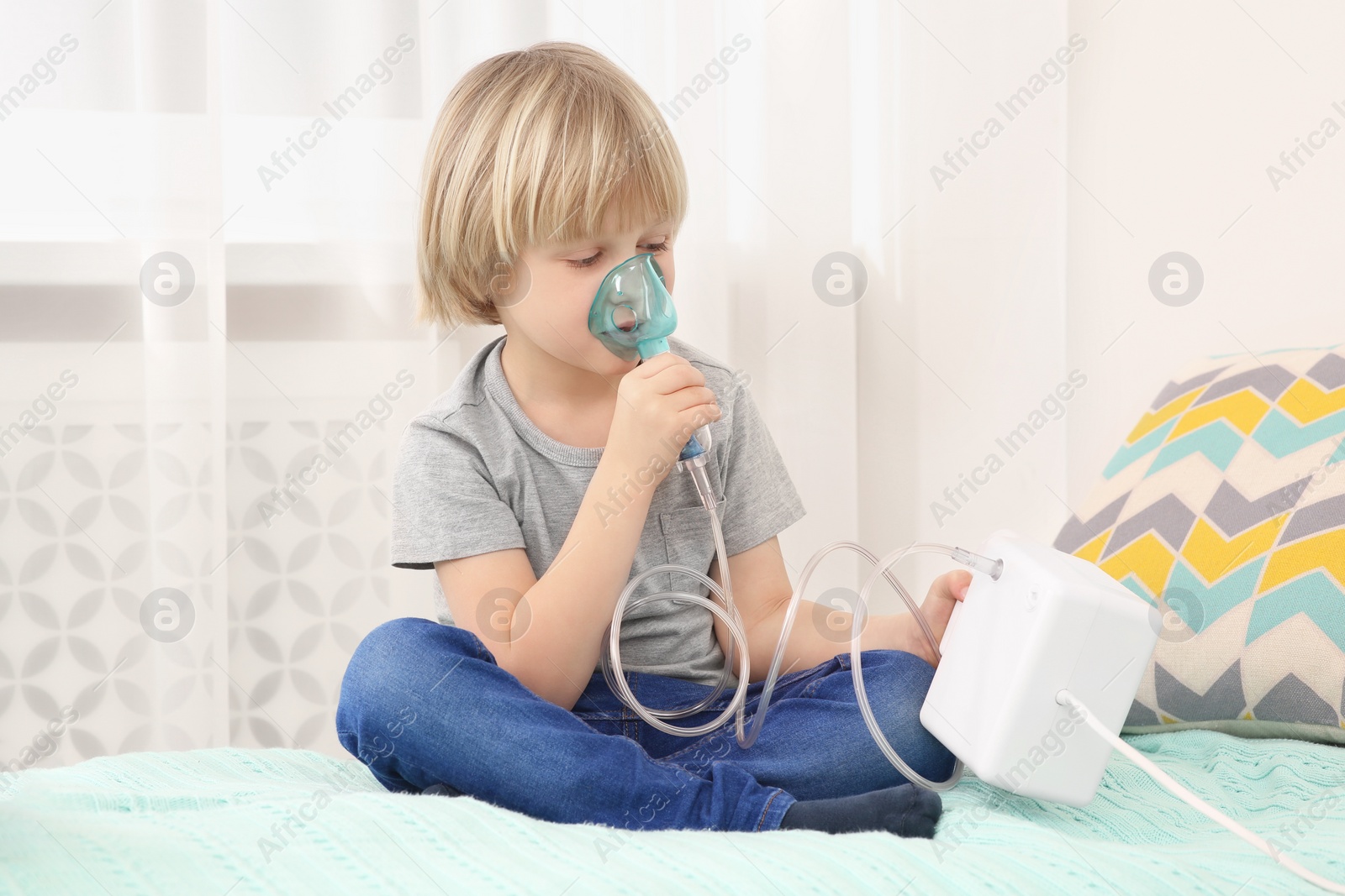 Photo of Sick little boy using nebulizer for inhalation on bed at home