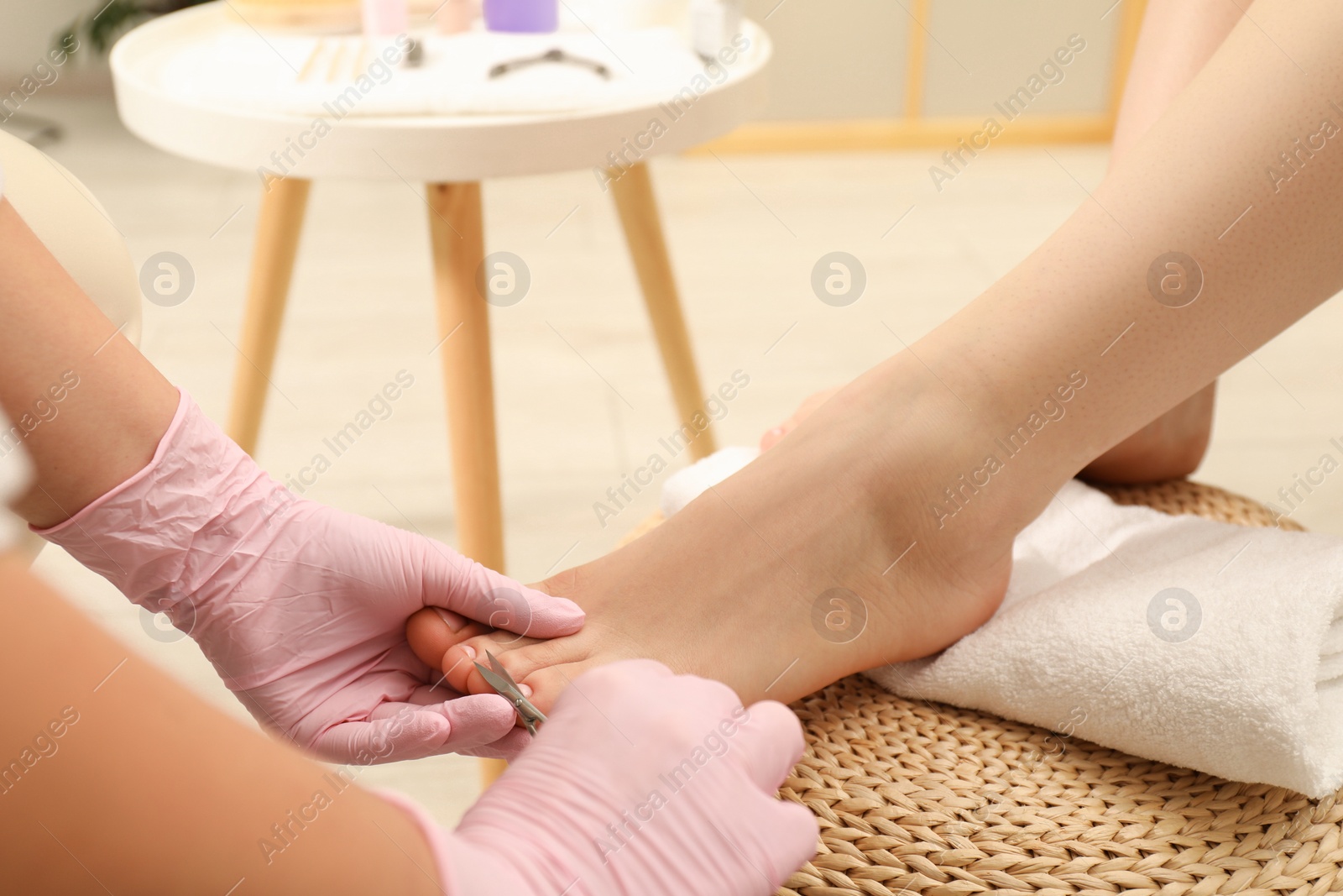 Photo of Professional pedicurist cutting client`s toenails with scissors in beauty salon, closeup