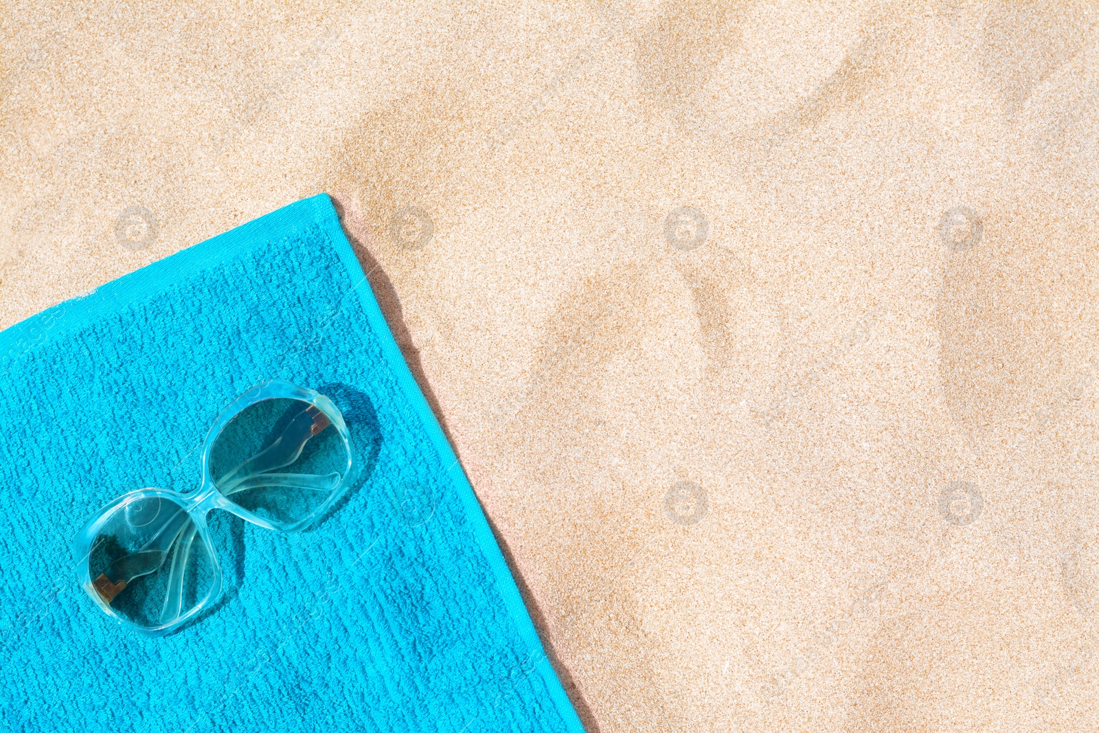 Photo of Soft blue beach towel with sunglasses on sand, top view. Space for text