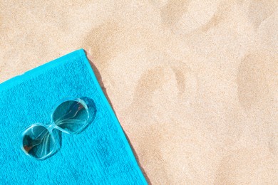 Soft blue beach towel with sunglasses on sand, top view. Space for text