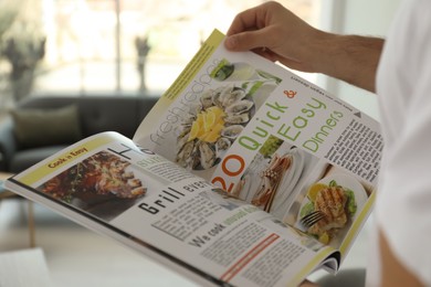 Photo of Man reading cooking magazine at home, closeup