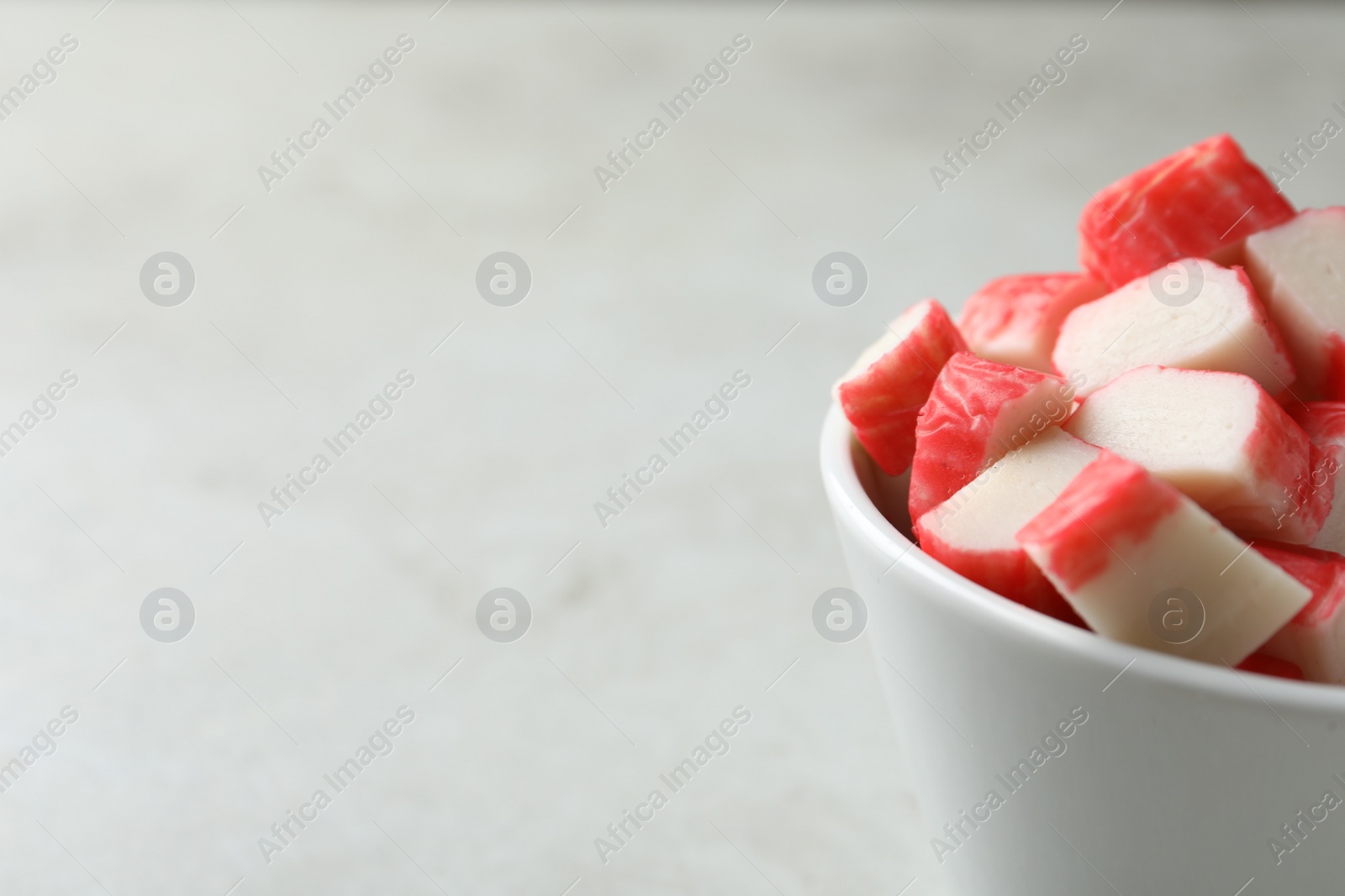 Photo of Cut crab sticks in bowl on light table, closeup. Space for text