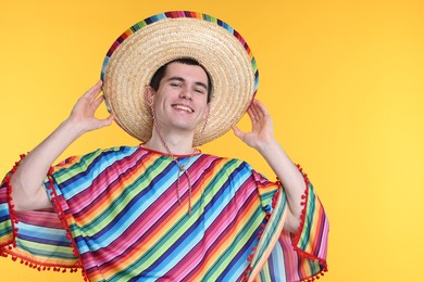 Photo of Young man in Mexican sombrero hat and poncho on yellow background