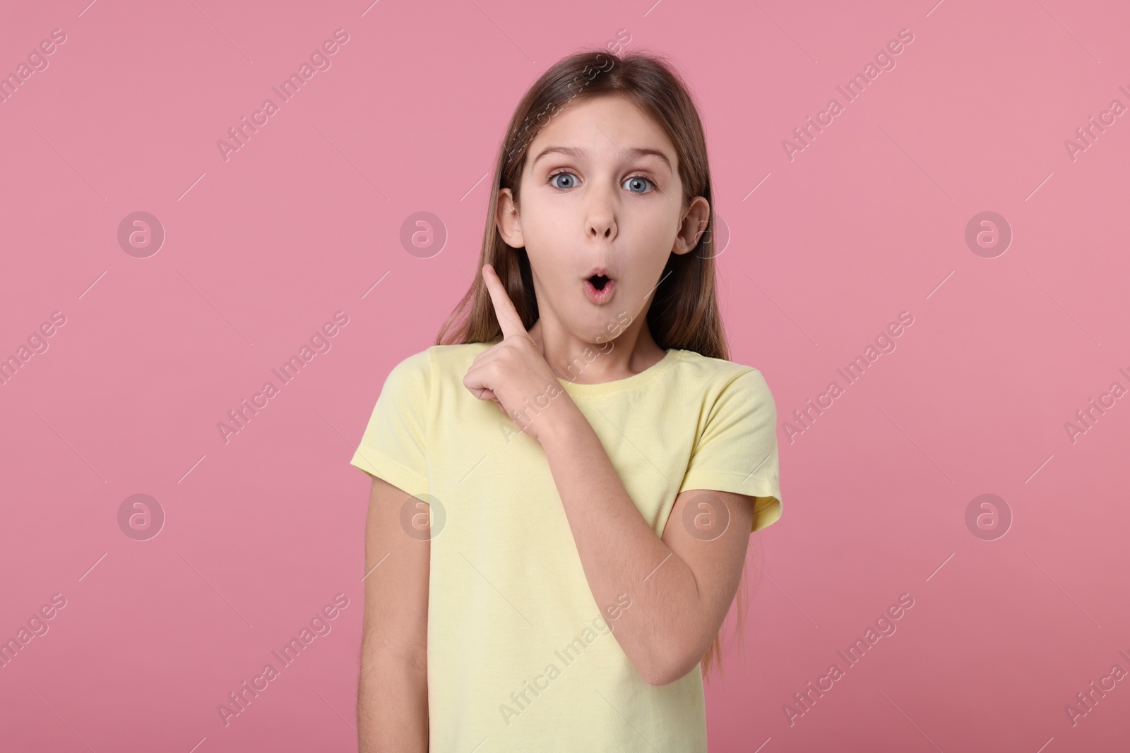 Photo of Surprised girl pointing at something on pink background