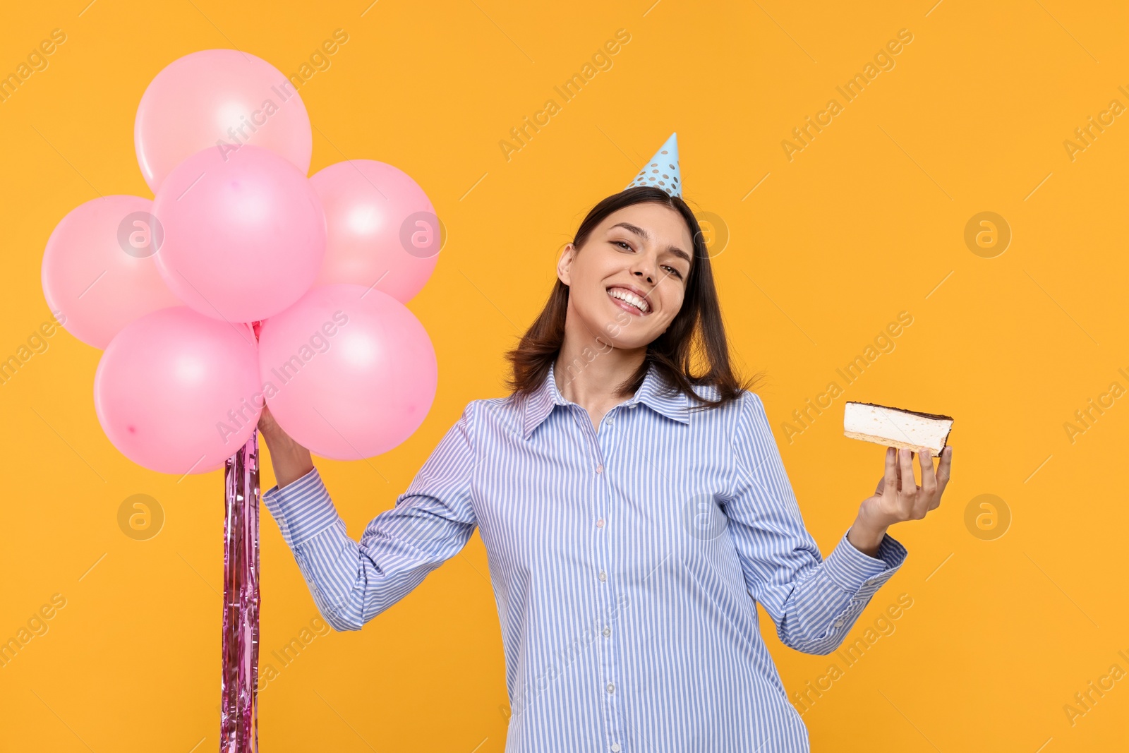 Photo of Happy young woman in party hat with balloons and cheesecake on yellow background