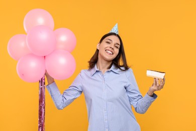Photo of Happy young woman in party hat with balloons and cheesecake on yellow background