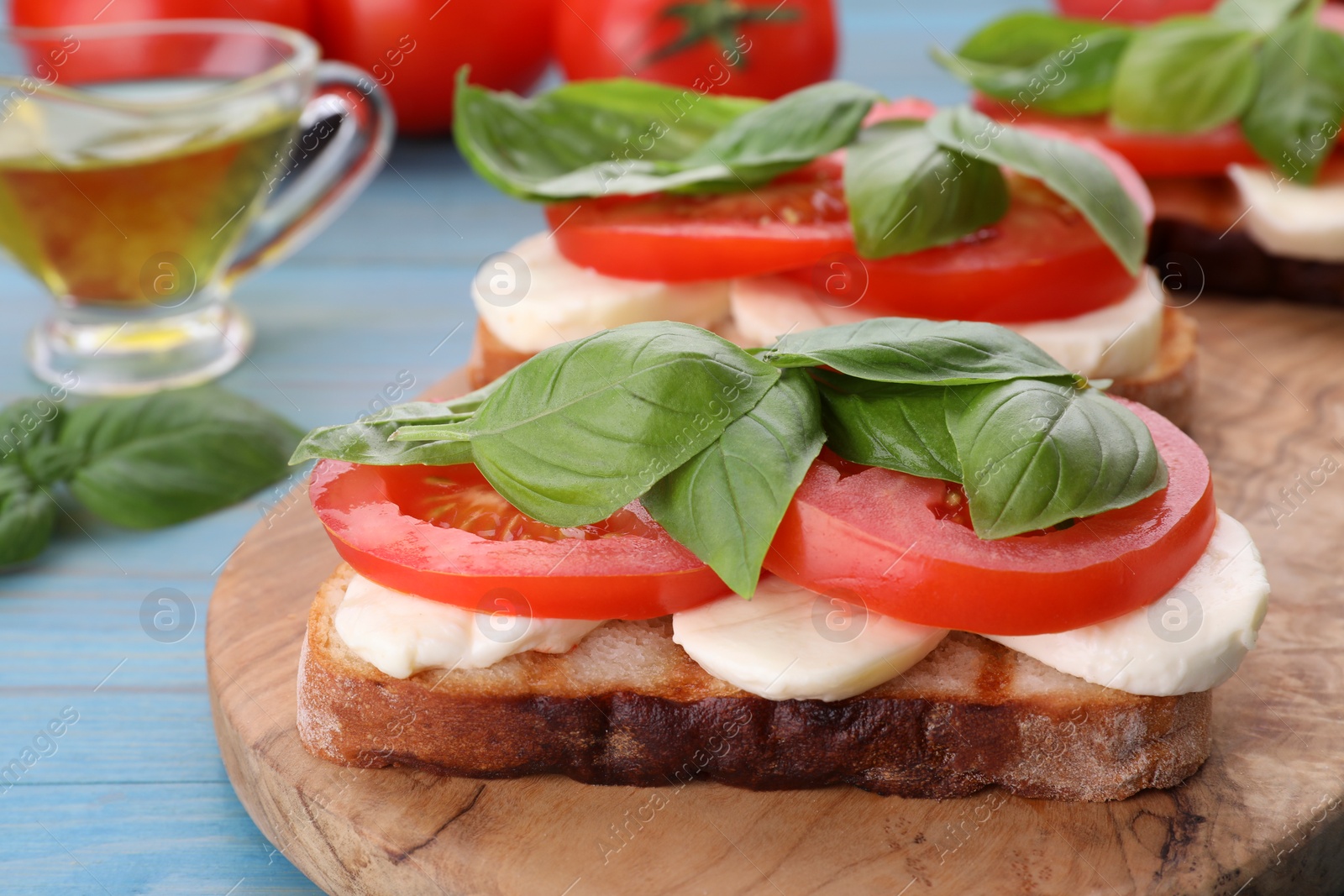 Photo of Delicious Caprese sandwiches with mozzarella, tomatoes and basil on light blue wooden table, closeup