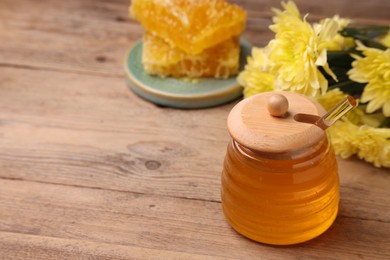 Photo of Sweet golden honey in jar and chrysanthemum flowers on wooden table, space for text