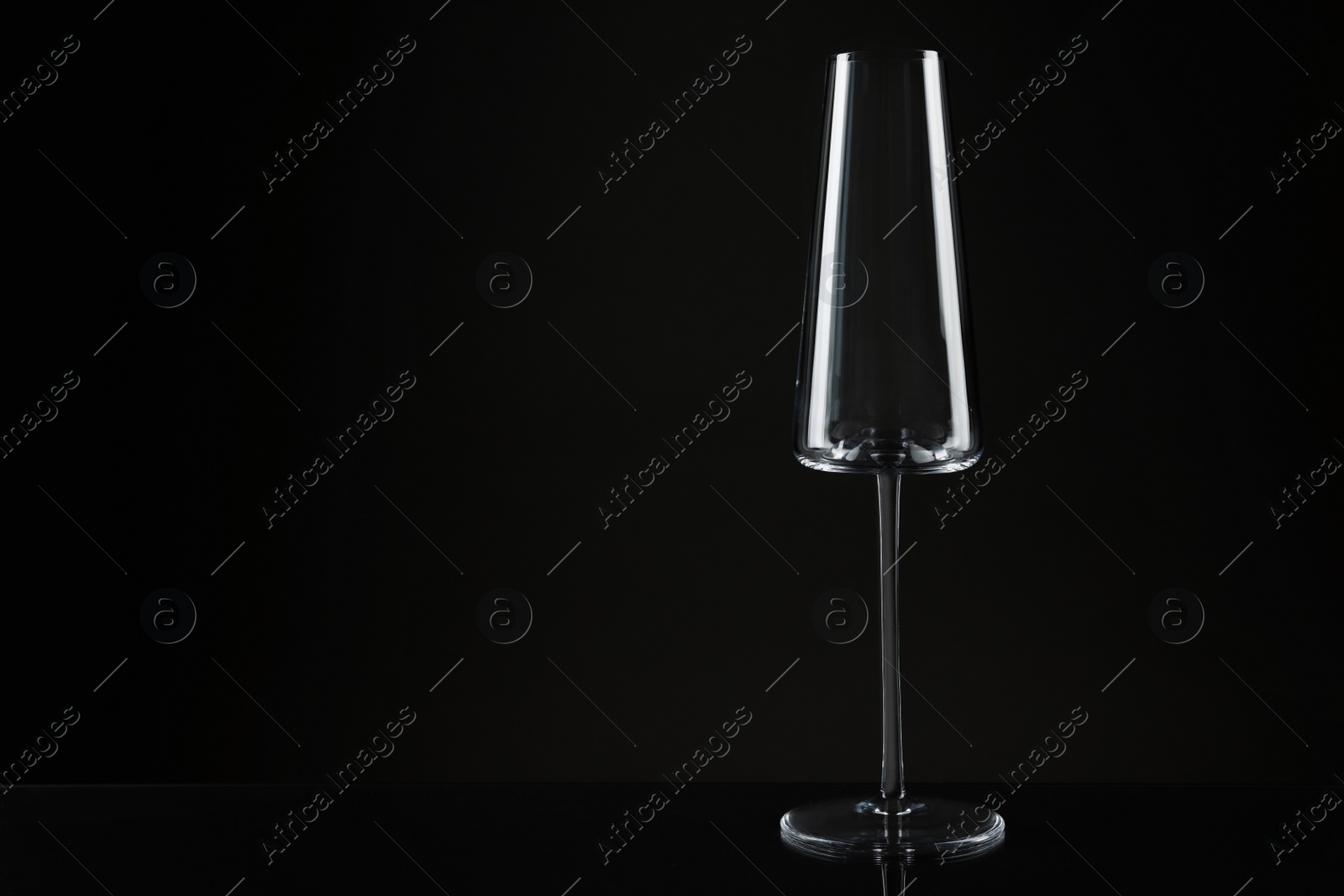 Photo of Empty glass for champagne on table against dark background. Space for text