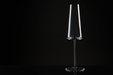 Photo of Empty glass for champagne on table against dark background. Space for text