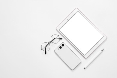 Modern tablet, smartphone and glasses on white background, flat lay. Space for text