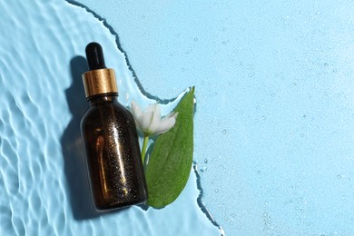 Photo of Bottle of cosmetic oil, green leaf and flower in water on light blue background, flat lay. Space for text
