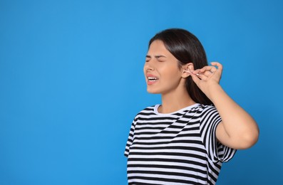 Photo of Young woman cleaning ear with cotton swab on light blue background, space for text