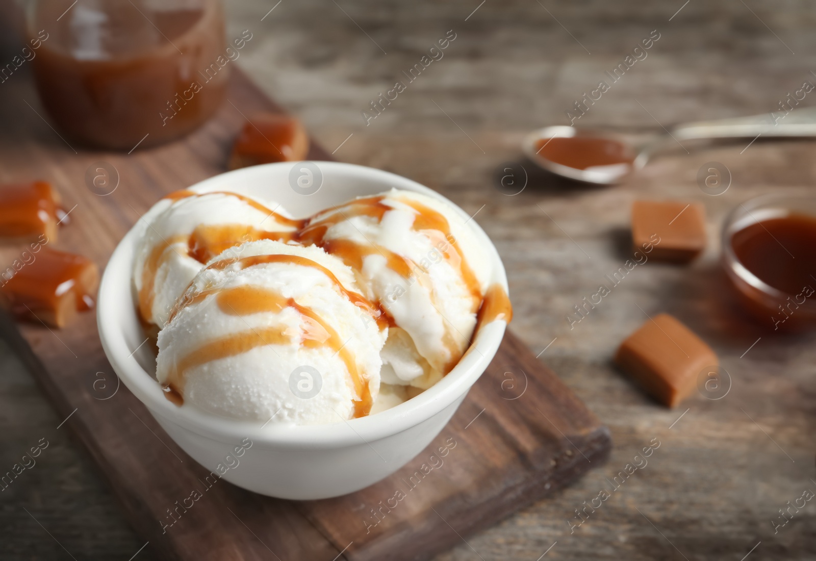 Photo of Tasty ice cream with caramel sauce in bowl on wooden board