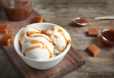 Tasty ice cream with caramel sauce in bowl on wooden board