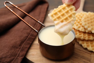 Photo of Woman dipping waffle into tasty condensed milk at table, closeup