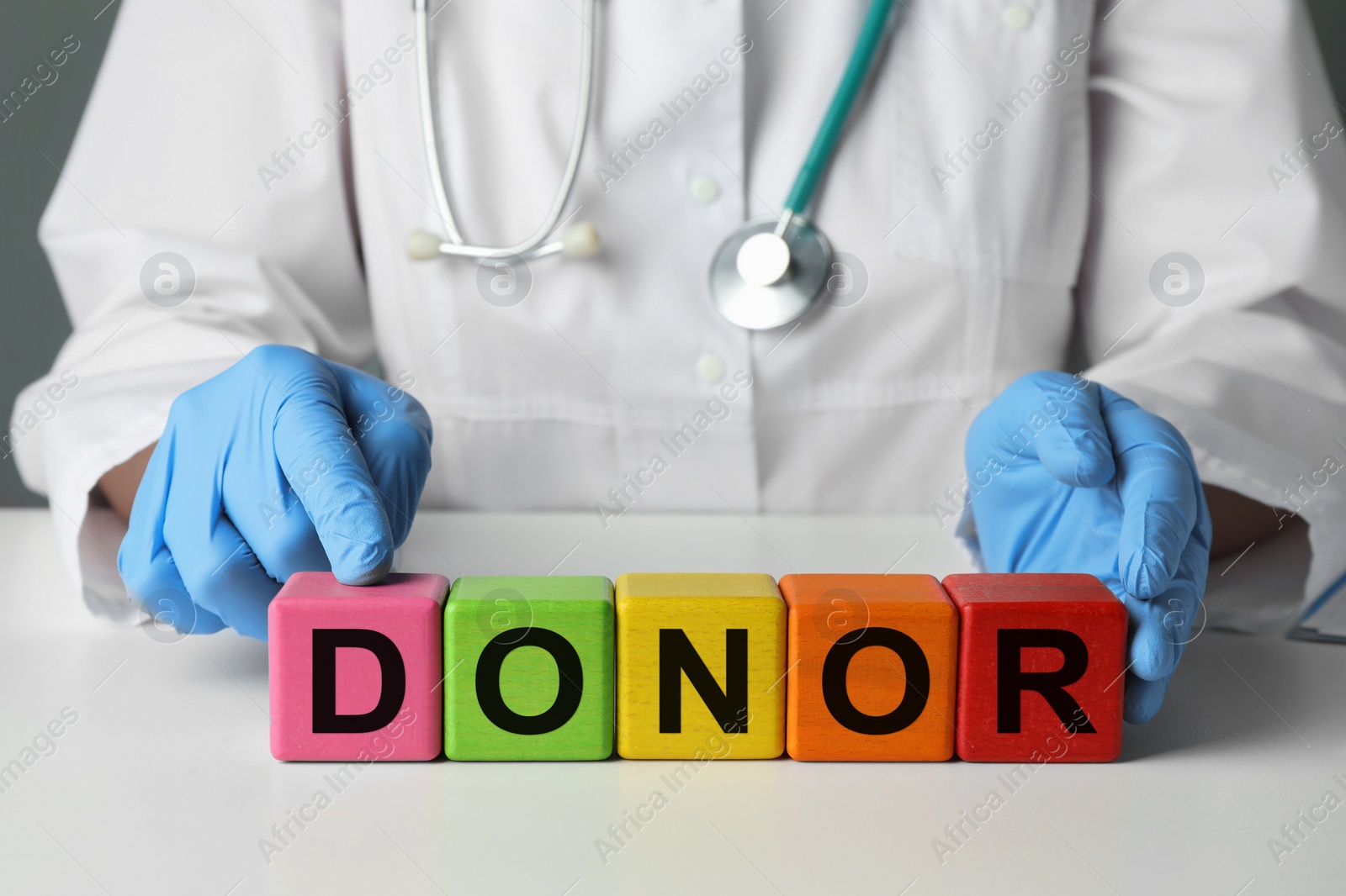 Photo of Doctor making word Donor of wooden cubes with letters at white table, closeup