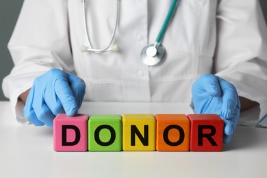 Doctor making word Donor of wooden cubes with letters at white table, closeup