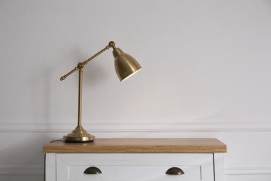 Photo of Wooden chest of drawers with modern lamp near white wall, space for text. Interior element