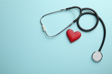 Photo of Stethoscope and red heart on light blue background, top view. Space for text