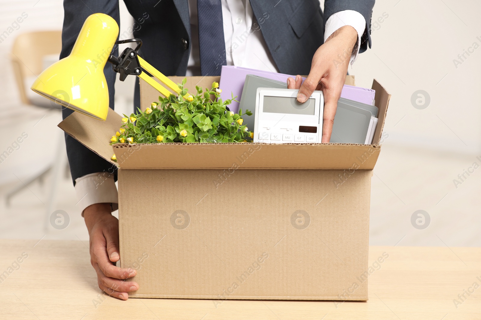 Photo of Unemployment problem. Man with box of personal belongings at table in office, closeup