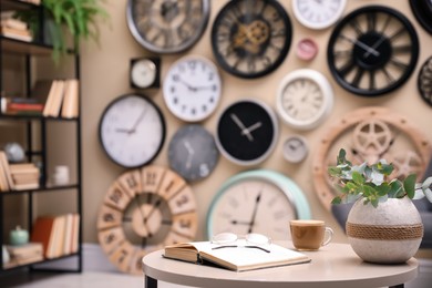 Photo of Open book, glasses, coffee and blurred view of wall with clocks on background