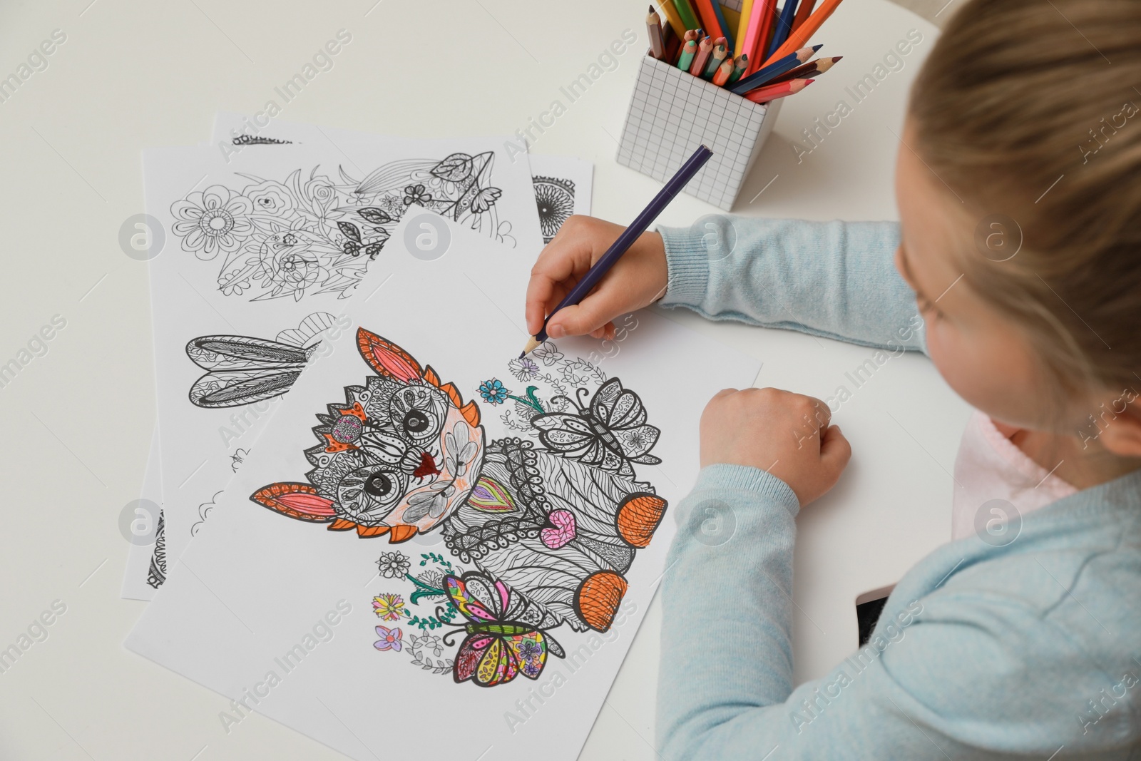 Photo of Little girl coloring antistress page at table, above view