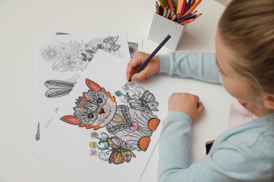 Little girl coloring antistress page at table, above view