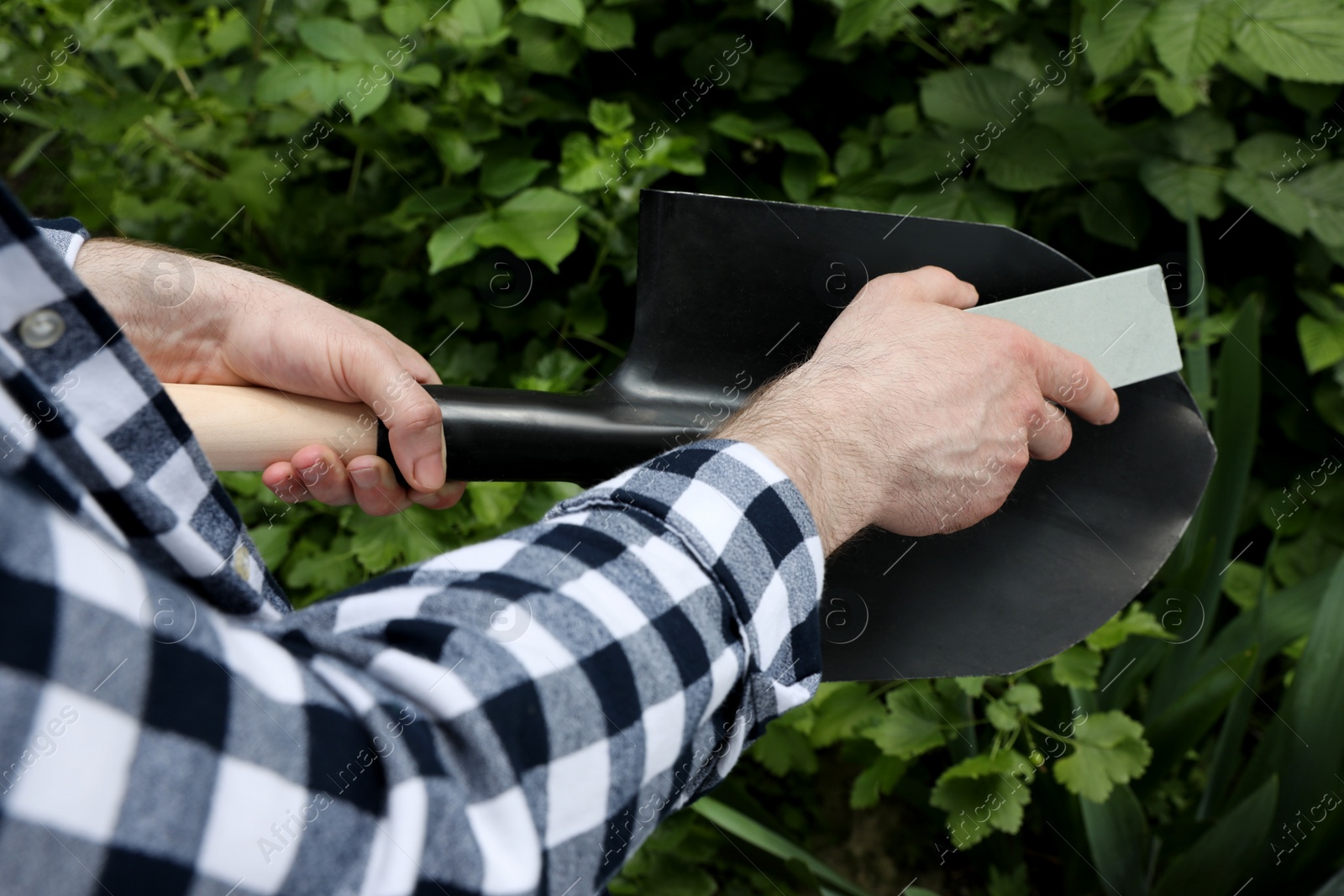 Photo of Man sharpening shovel outdoors, closeup. Gardening tools