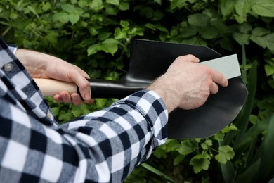 Photo of Man sharpening shovel outdoors, closeup. Gardening tools