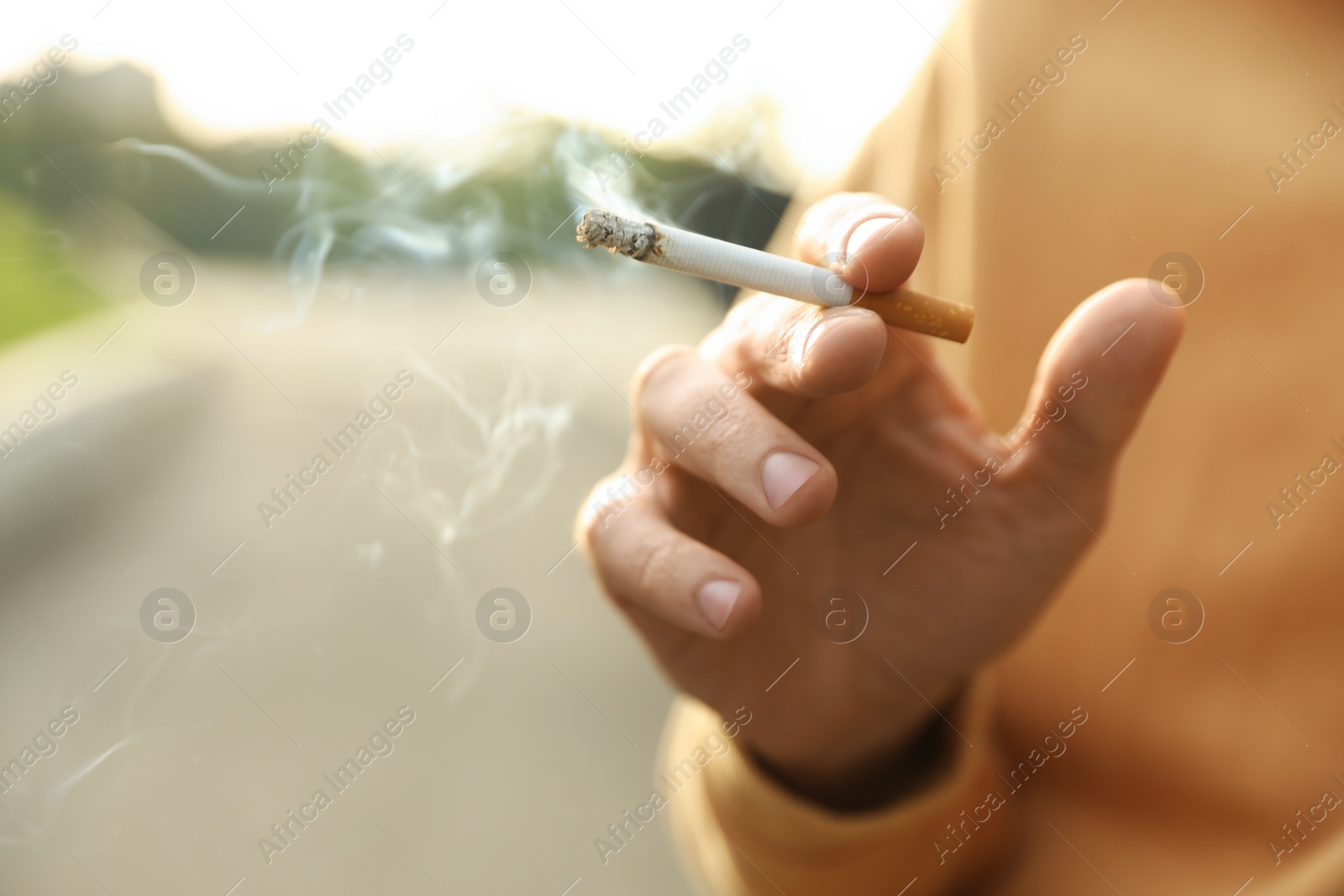 Photo of Man with cigarette outdoors, closeup of hand. Space for text