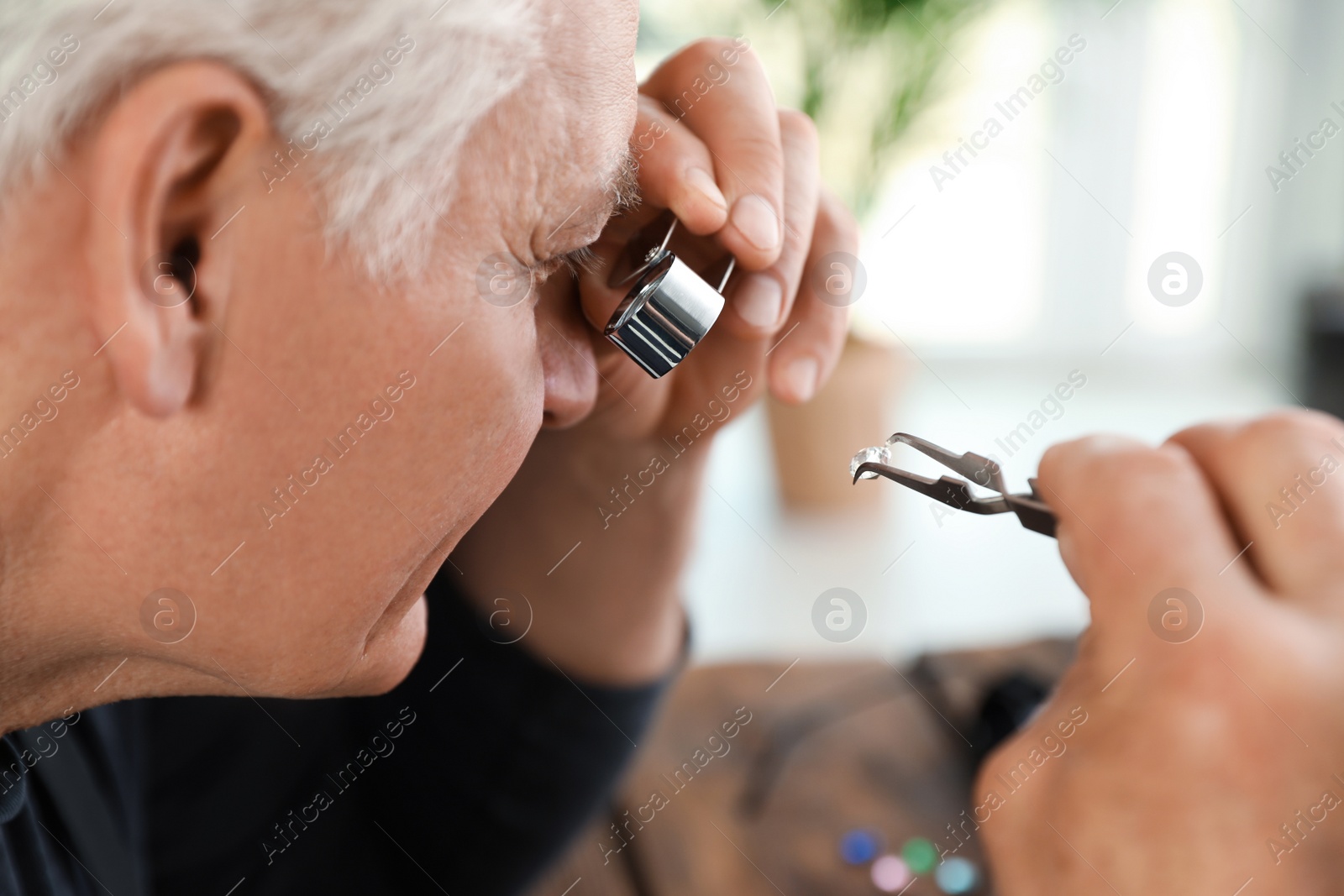 Photo of Male jeweler evaluating precious gemstone in workshop, closeup