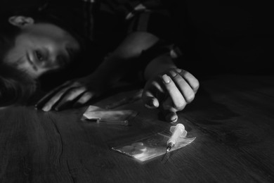 Photo of Addicted woman lying indoors, focus on different drugs. Black and white effect
