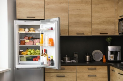 Photo of Open refrigerator full of products in kitchen