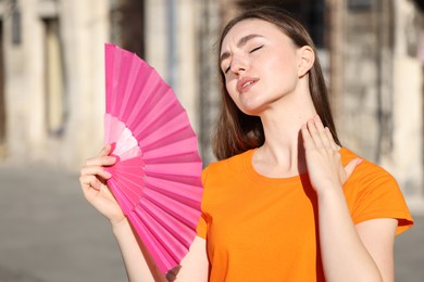 Woman with hand fan suffering from heat outdoors