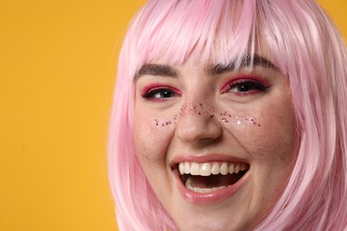 Photo of Happy woman with bright makeup and glitter freckles on yellow background, closeup. Space for text