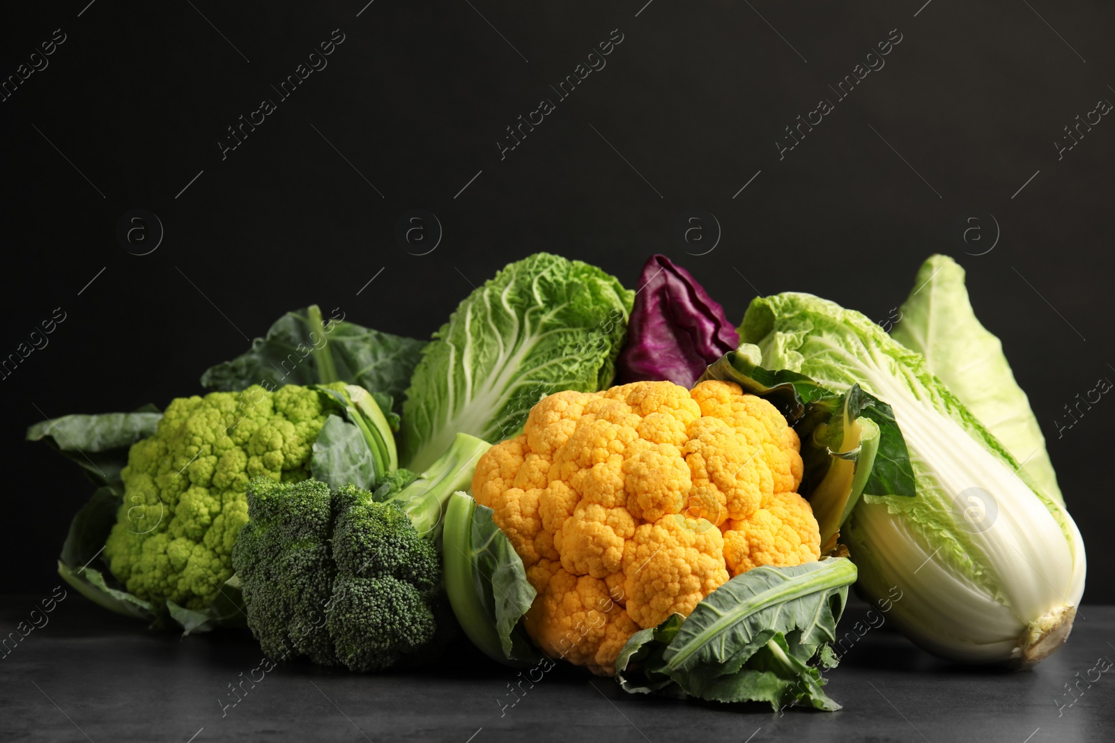 Photo of Different fresh cabbages on table against black background. Healthy food