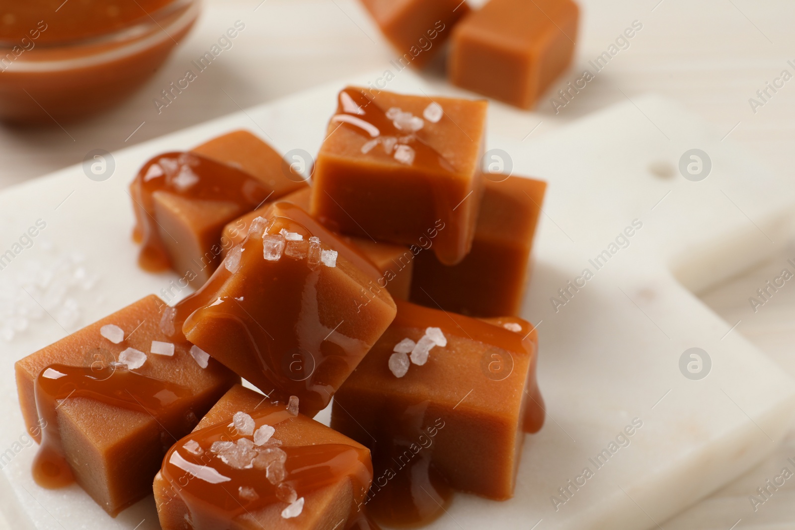 Photo of Tasty caramel candies with sauce and sea salt on white table, closeup