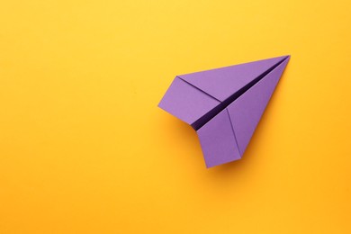 Handmade purple paper plane on yellow background, top view. Space for text