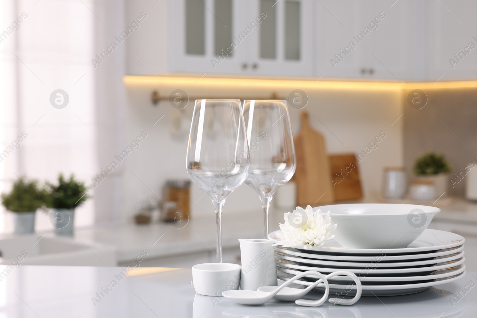 Photo of Set of clean dishware, glasses and flower on table in kitchen, space for text