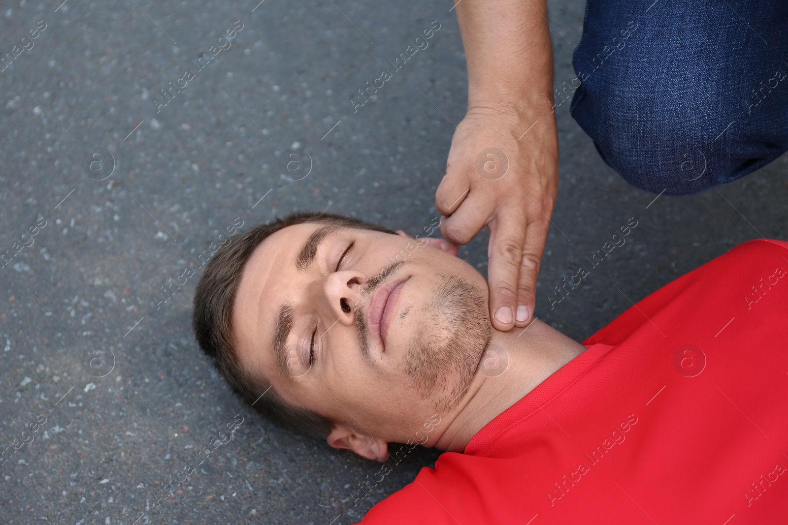 Photo of Passerby checking pulse of unconscious young man outdoors