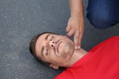 Passerby checking pulse of unconscious young man outdoors