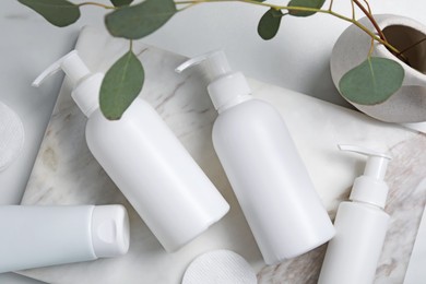 Different face cleansing products and eucalyptus leaves on white table, flat lay