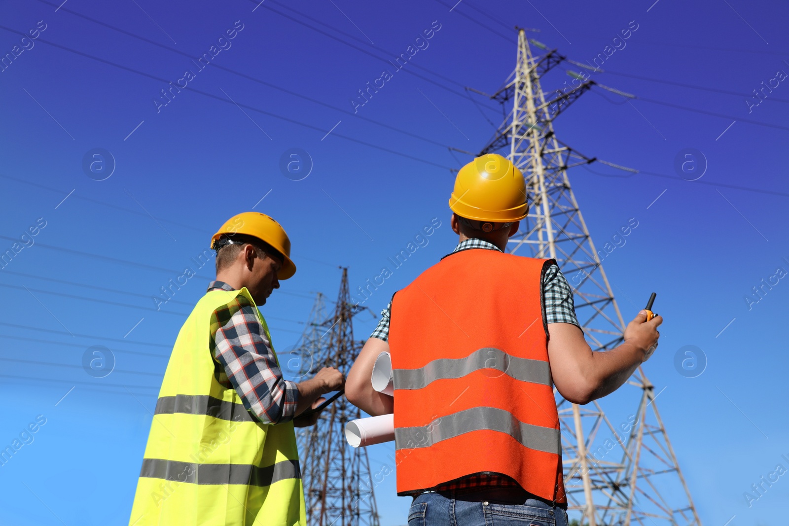 Photo of Professional electricians in uniforms near high voltage towers