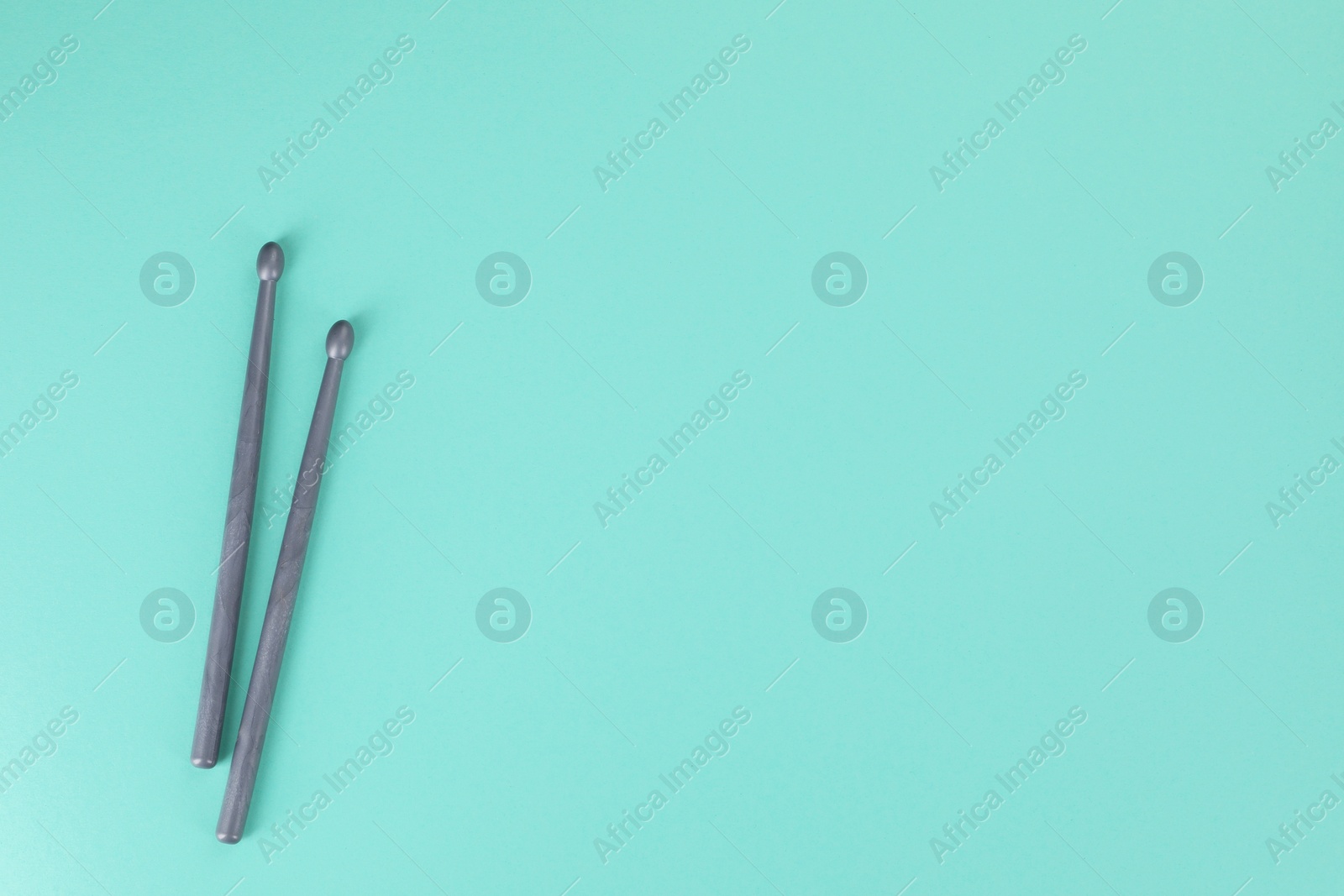 Photo of Two grey drumsticks on turquoise background, top view. Space for text