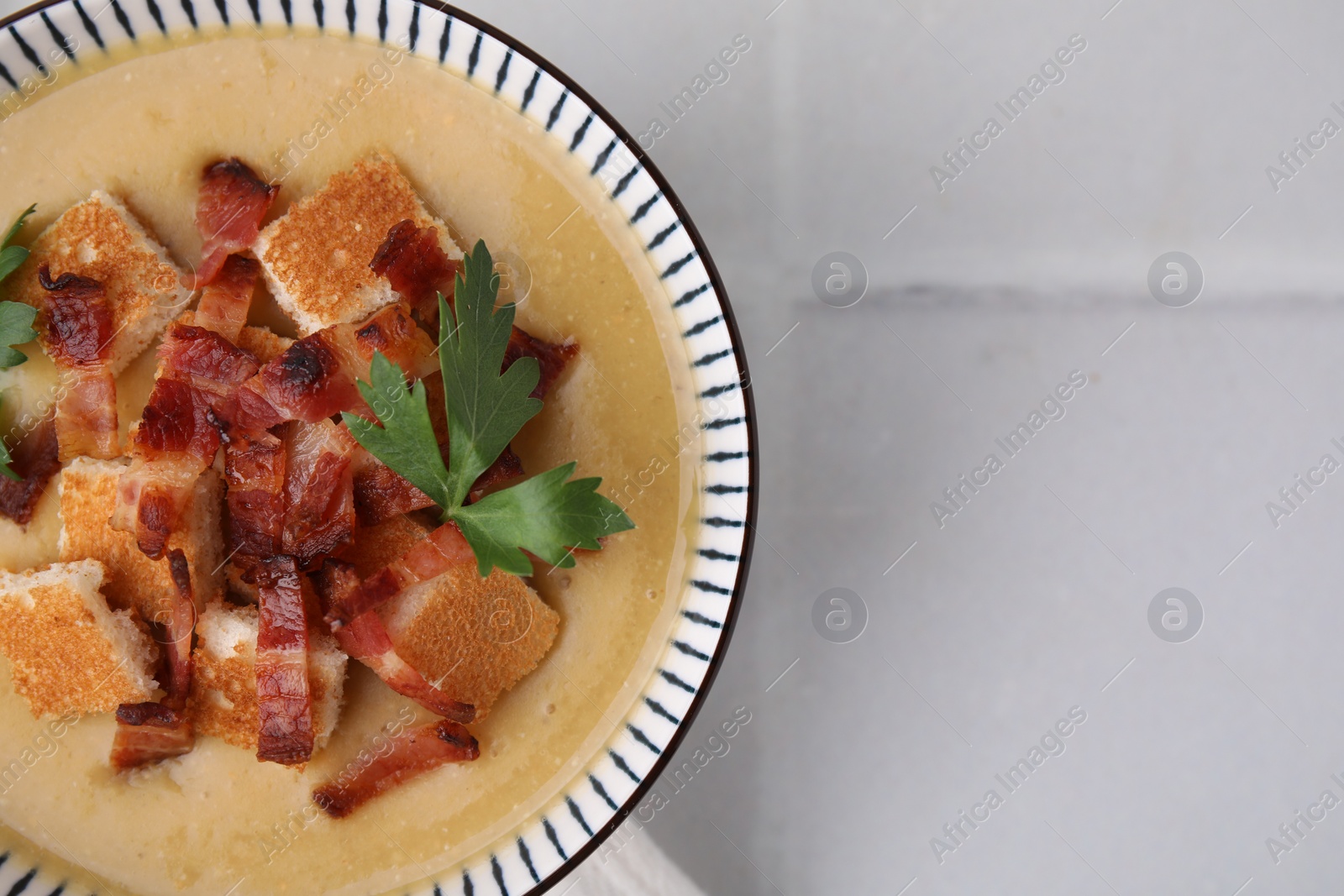 Photo of Delicious lentil soup with bacon and parsley in bowl on light table, top view. Space for text