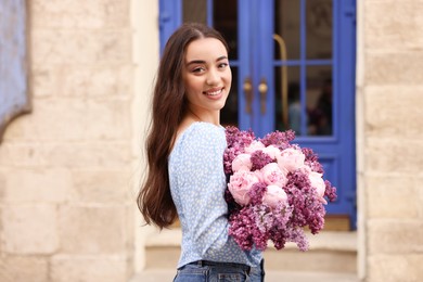 Photo of Beautiful woman with bouquet of spring flowers near building outdoors